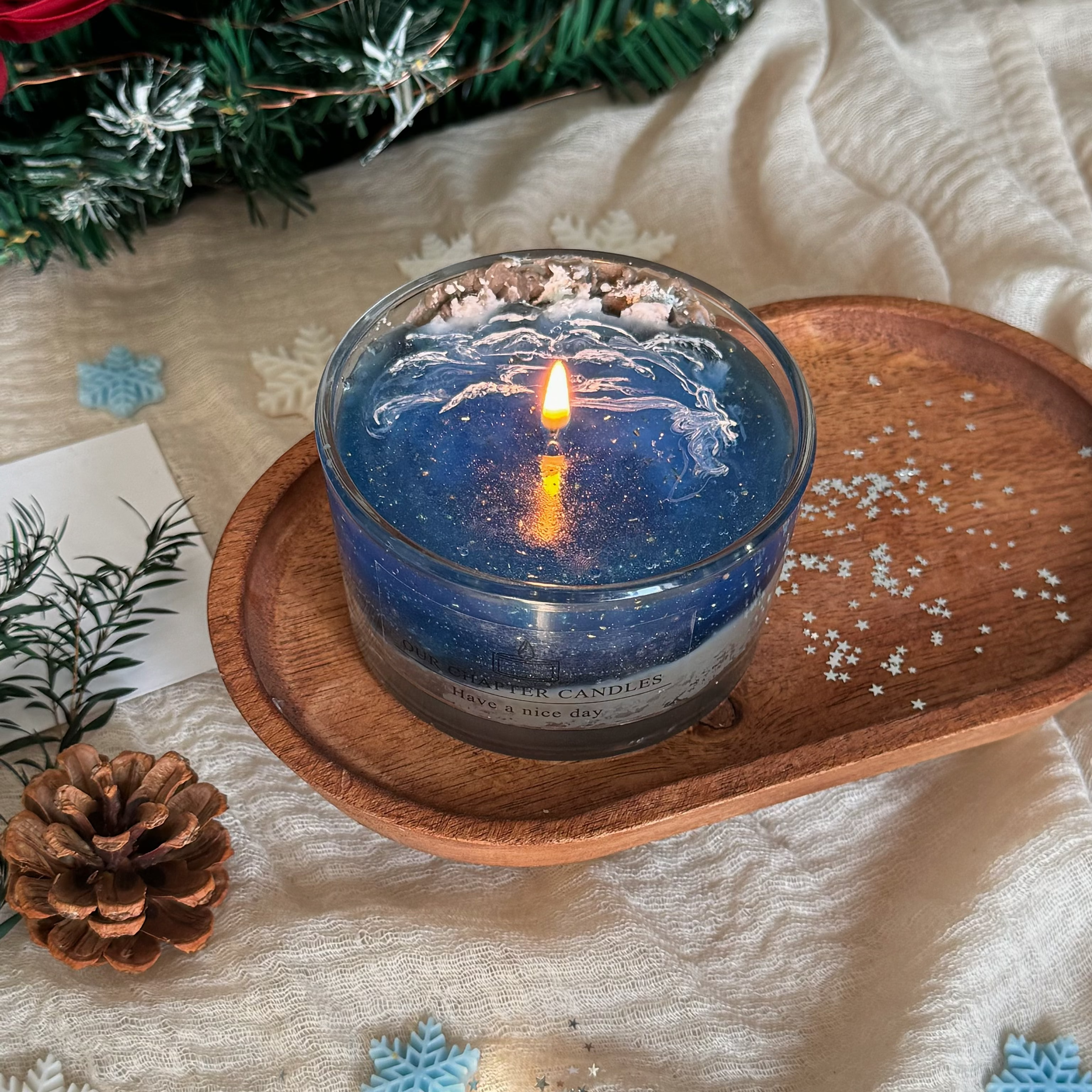 Cozy winter holiday ambient scene featuring a burning starry night gel candle surrounded by pinecones, snowflakes, and a Christmas tree. Perfect aesthetic home fragrance gift idea for festive celebrations.