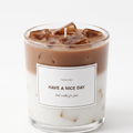 Aesthetic light brown iced coffee latte scented candle inside a clear glass vessel topped with shimmering gel wax ice cubes. Premium beverage-style gift candle with a "THANK YOU" message on a pure white background.