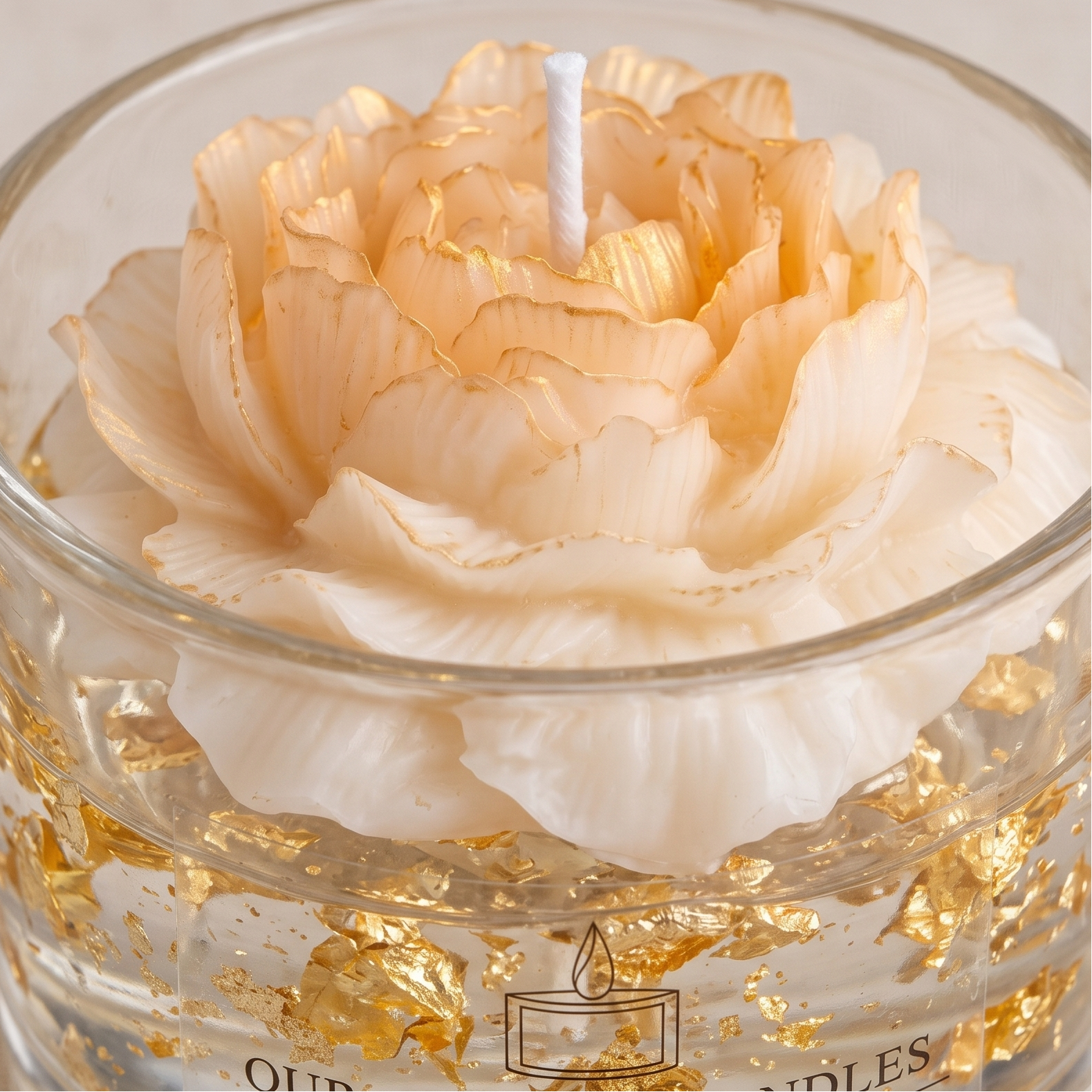 Extreme close-up shot of hand-sculpted cream and gold gradient wax flower petals. Macro view of a luxury candle showing detailed texture of suspended gold leaf flakes in clear wax and sharp branded typography on the glass.