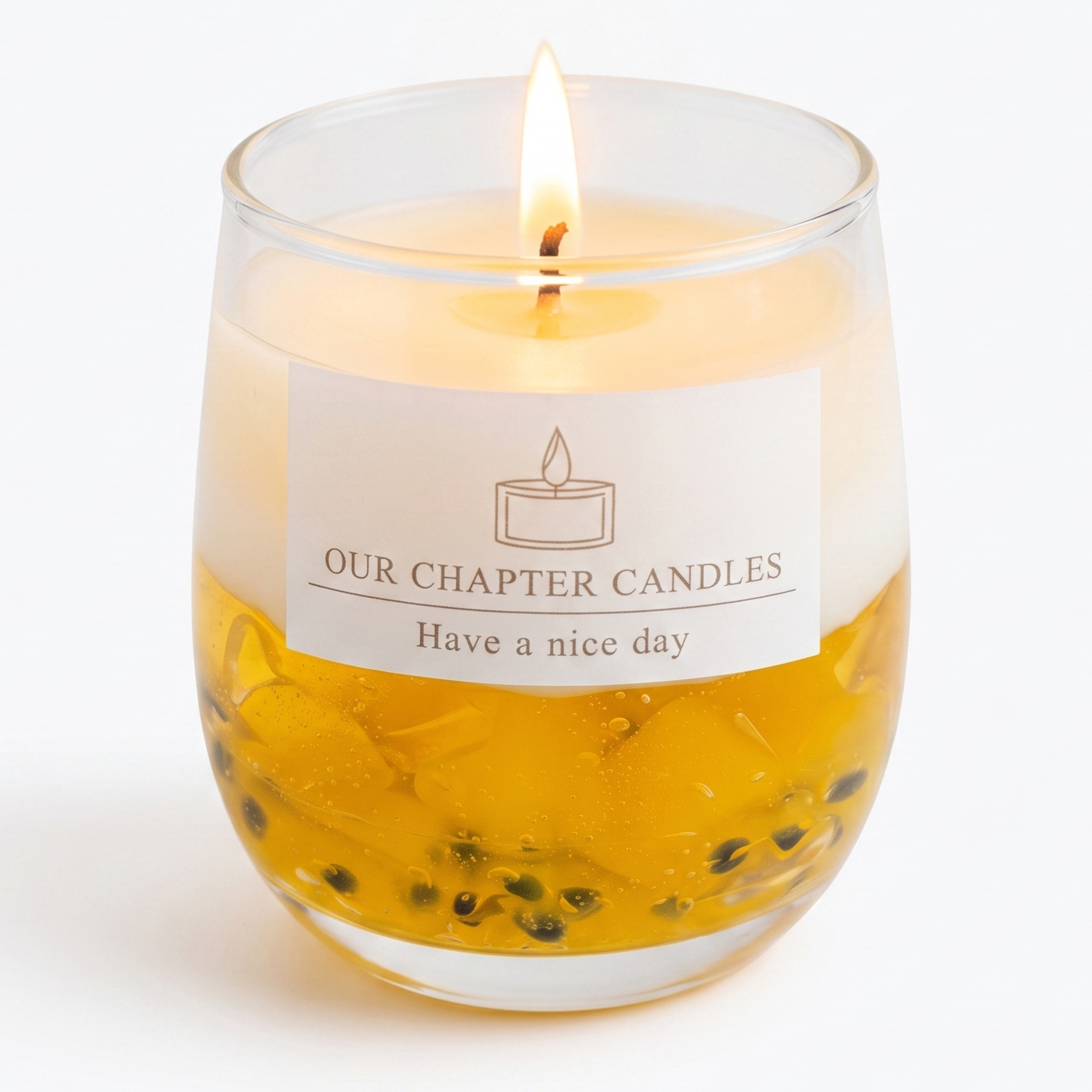 Extreme macro close-up of a lit dessert candle showcasing the glossy waxy texture of translucent yellow gel wax and embedded black passion fruit seeds. High-resolution view of the glowing flame and clean rectangular "OUR CHAPTER CANDLES" label.