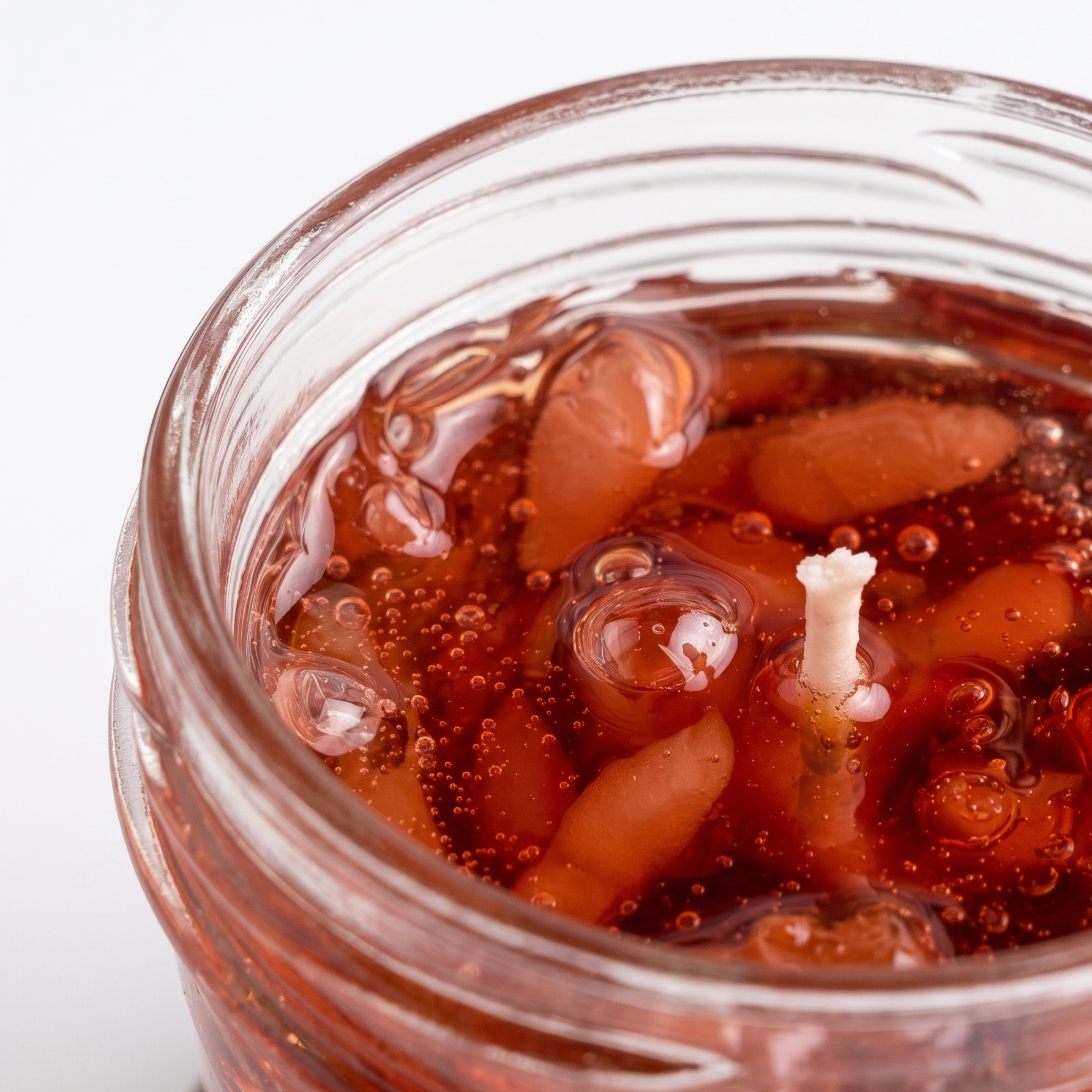 Extreme macro close-up of a botanical jelly candle showcasing the glossy waxy texture of translucent red-brown strawberry jam. High-resolution top view of realistic wax fruit pulp and shimmering air bubbles with a sharp central cotton wick.