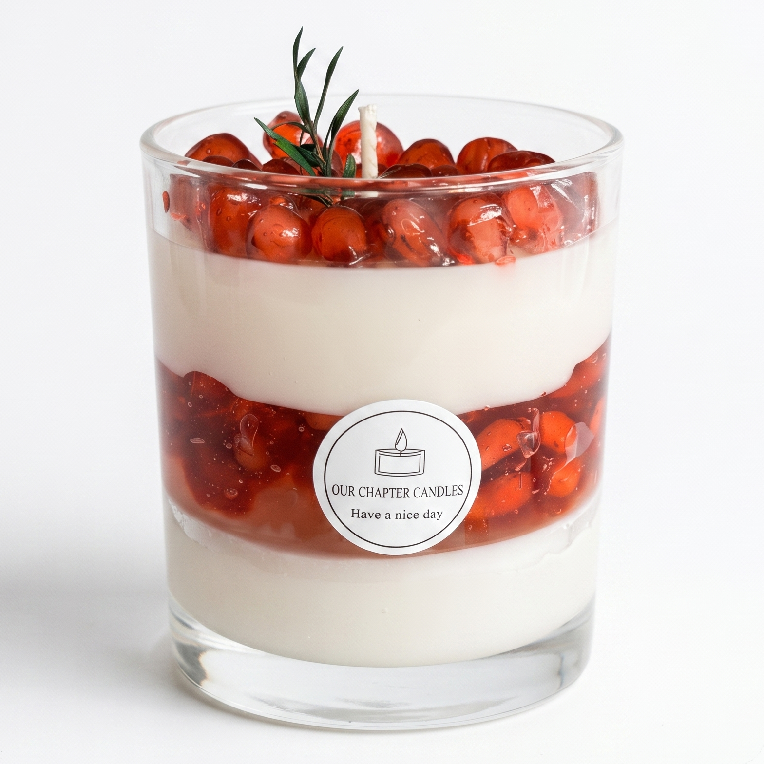 A luxury multi-layered pomegranate dessert parfait soy and gel wax candle in a clear glass jar based on image_3a0a3a.jpg. Features distinct white wax layers, a translucent red jelly fruit layer, and a top pile of realistic ruby wax seeds with a green rosemary sprig on a white background.